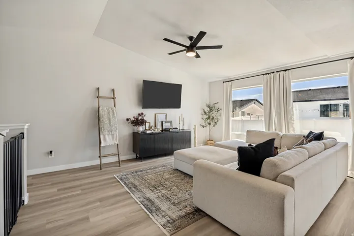 Vaulted ceiling with an attached ceiling fan, recessed wall for television, wood-finish flooring, and multiple windows with curtain rods