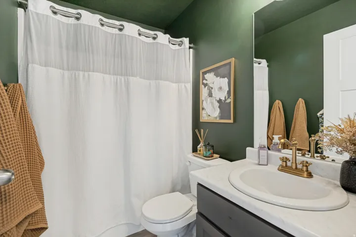 Integrated sink with gold-finish faucet, dark vanity with white countertop, full-height mirror, and white toilet