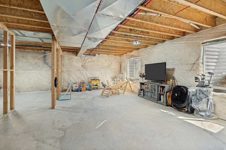 Unfinished basement with concrete flooring, exposed wood framing, and visible ductwork