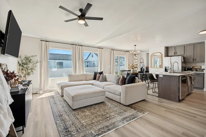 Open-concept living space featuring wood-finish flooring, a contemporary ceiling fan, and multiple windows with ample natural light