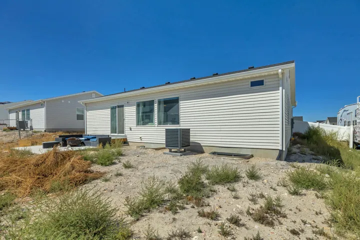 White horizontal siding, sliding glass door, multiple large windows, and a concrete patio