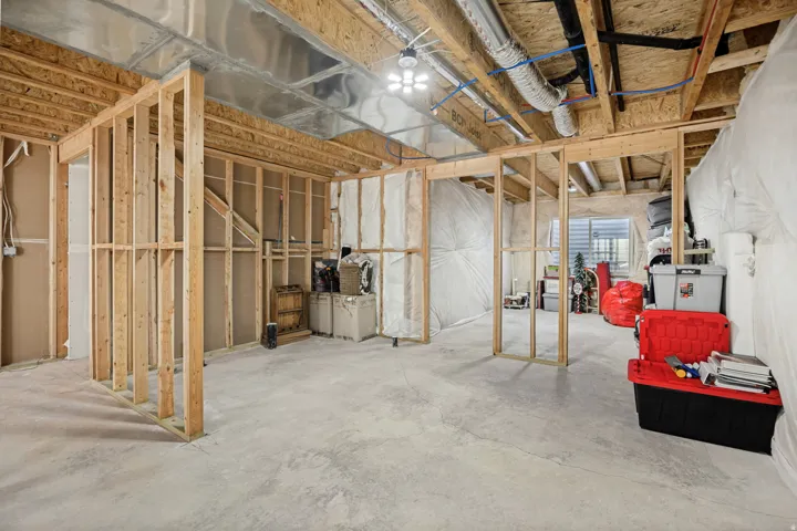 Unfinished basement with exposed wood framing, concrete flooring, and visible overhead utility lines