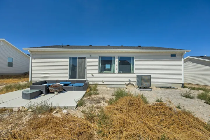 Rear exterior featuring white horizontal siding, a concrete patio, a sliding glass door, multiple windows, and a black shingled roof