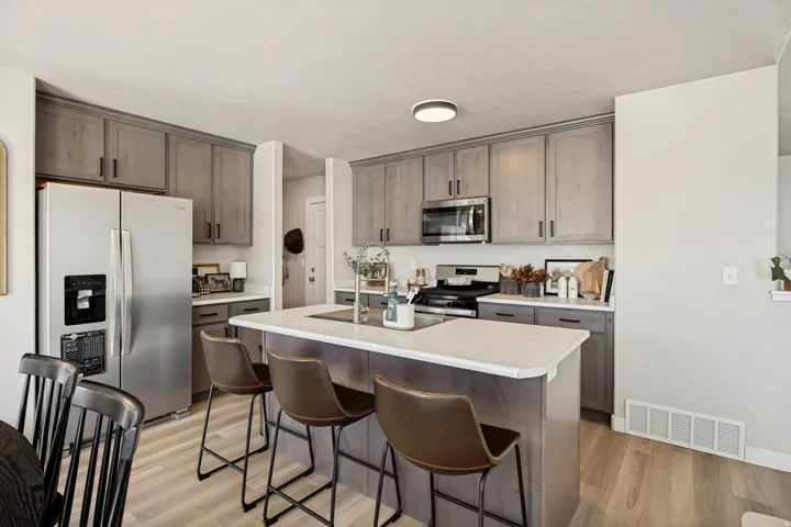 Kitchen featuring a large island with sink, stainless steel appliances, wood-finish flooring, and gray cabinetry with black hardware