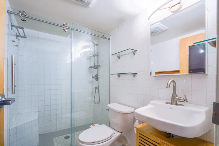 Shower with a built-in bench and sliding glass door, white square tile walls, wall-mounted sink with a brushed nickel faucet, and a medicine cabinet with integrated lighting