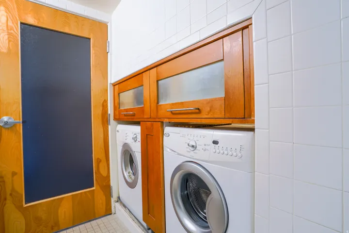 White tile walls, wood-finish cabinetry with frosted glass inserts, and a wood-finish door with a dark panel