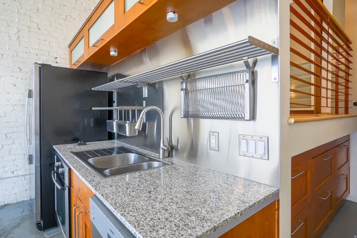 Compact kitchen featuring a double basin sink, stainless steel backsplash, and granite-style countertop