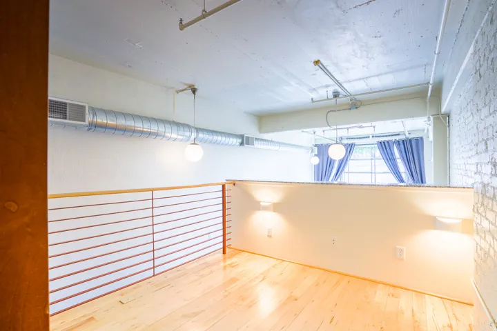 Hardwood-style flooring, exposed ductwork, industrial lighting, brick accent wall, and contemporary railing