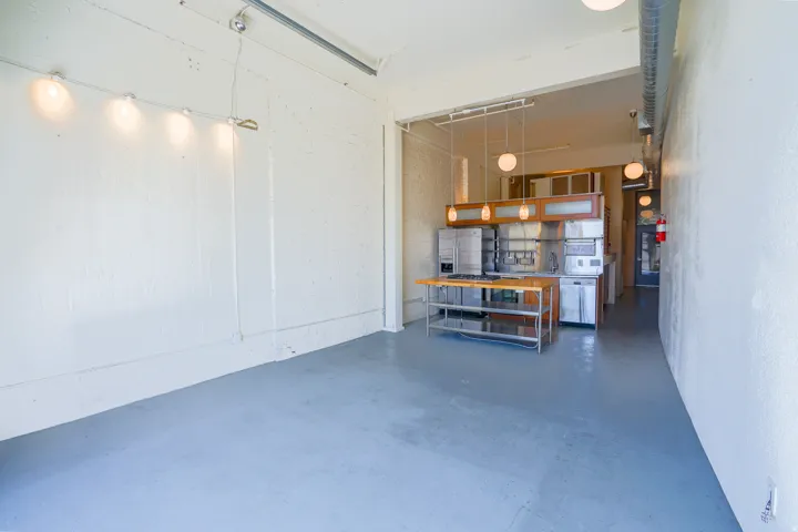 Open-concept space with a concrete floor, track lighting, and a built-in kitchen area featuring wood-finish cabinetry and stainless steel appliances
