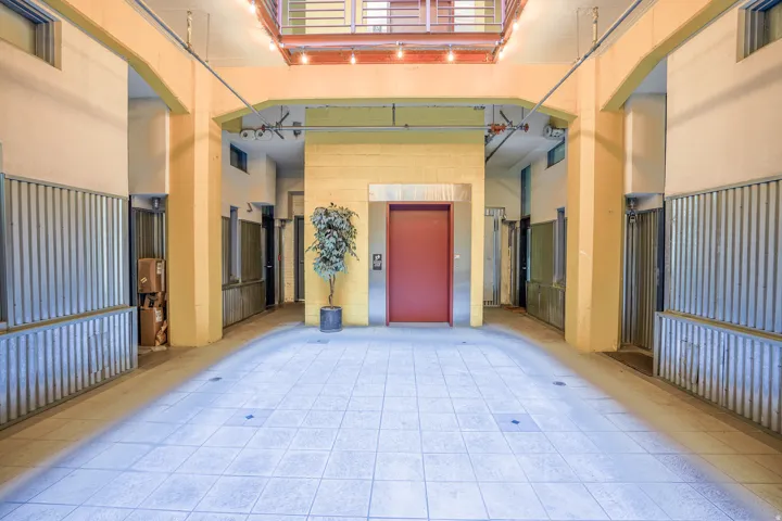 Tiled flooring, red elevator door, exposed conduit, corrugated metal paneling, and a second-story walkway with railings