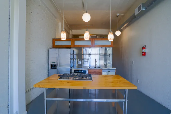 Kitchen featuring stainless steel appliances, wood-finish cabinetry with frosted glass inserts, a stainless steel backsplash, and a butcher block island with a built-in gas cooktop