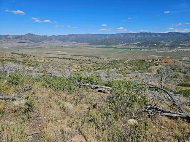 Expansive mountain landscape with a broad valley, distant structures, and open terrain