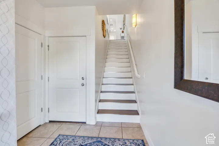 Tiled flooring entry with white doors and a staircase featuring wood-finish treads
