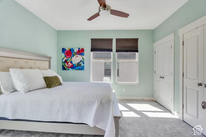 Carpeted flooring, two windows with blinds, a ceiling fan, and two white bi-fold doors