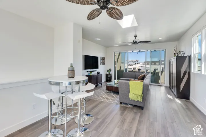 Living area featuring wood-finish flooring, two ceiling fans, a skylight, and sliding glass doors