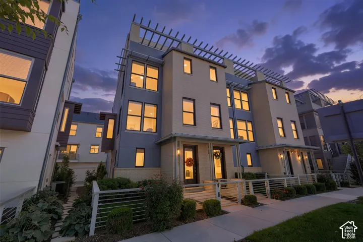 Contemporary multi-level townhome architecture with a contrasting material palette, decorative pergolas, multiple large windows, and a private fenced front patio