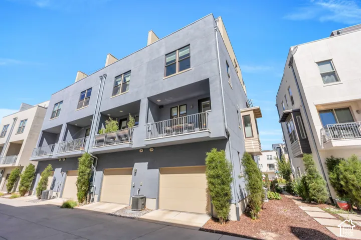 Contemporary multi-level townhome featuring a stucco exterior, multiple private balconies with metal railings, and attached garage access