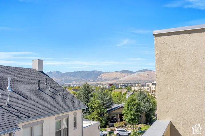 Distant mountain range, expansive blue sky, residential rooftops, lush green trees, and stucco exterior