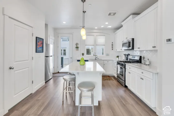 White cabinetry with brushed nickel hardware, stainless steel appliances, a center island with countertop seating, wood-finish flooring, and a subway tile backsplash