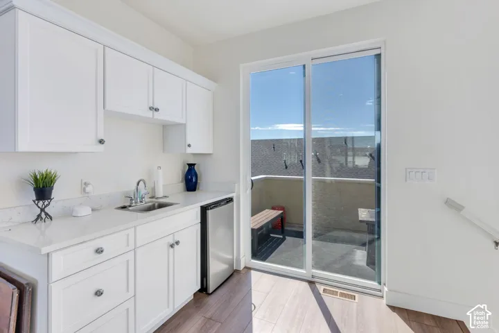 White shaker-style cabinetry, stainless steel sink, light-toned countertop, wood-finish flooring, and sliding glass doors to outdoor space