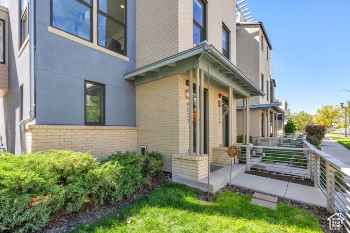 Contemporary exterior featuring light brick and stucco, a covered entry porch, and a metal railing alongside the walkway