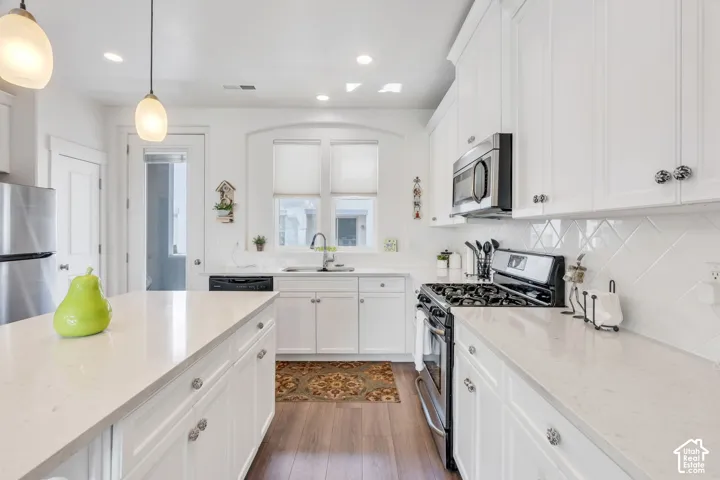 White cabinetry, light-toned countertops, stainless steel appliances, white tile backsplash, and wood-finish flooring
