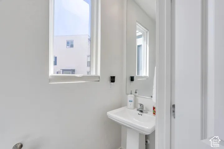 Pedestal sink with chrome faucet, a rectangular mirror, and a window with a roller blind