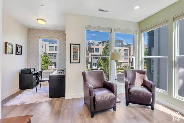 Wood-finish flooring throughout, large windows with roller blinds, and a built-in desk with a window overlooking the surroundings