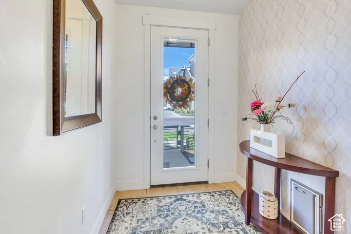 Wood-frame mirror, white walls, full-light entry door, patterned accent wall, and tile flooring