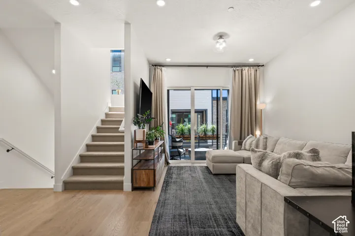 Recessed lighting, wood-finish flooring, and a carpeted staircase with a view of the covered patio