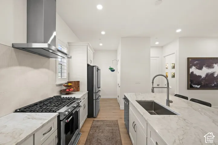 Modern kitchen featuring stainless steel appliances, granite countertops, white cabinetry, light-toned wood-finish flooring, a kitchen island with an undermount sink, and recessed lighting
