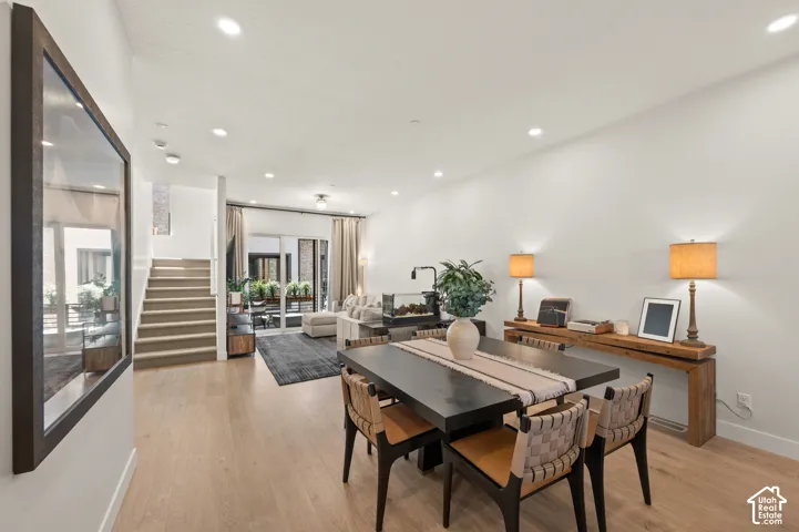 Open-concept living space with light wood-finish flooring, recessed ceiling lighting, a contemporary staircase, and glass panel doors to outdoor patio.