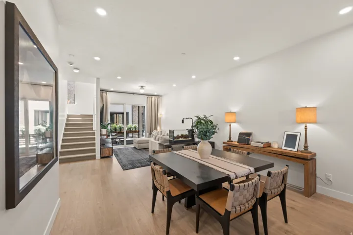 Open-concept living space with light wood-finish flooring, recessed ceiling lighting, a contemporary staircase, and glass panel doors to outdoor patio.