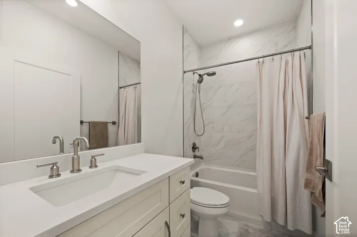 Light-toned quartz countertops with cabinet storage, large vanity mirror, white bathtub with shower, and marble-patterned shower surround