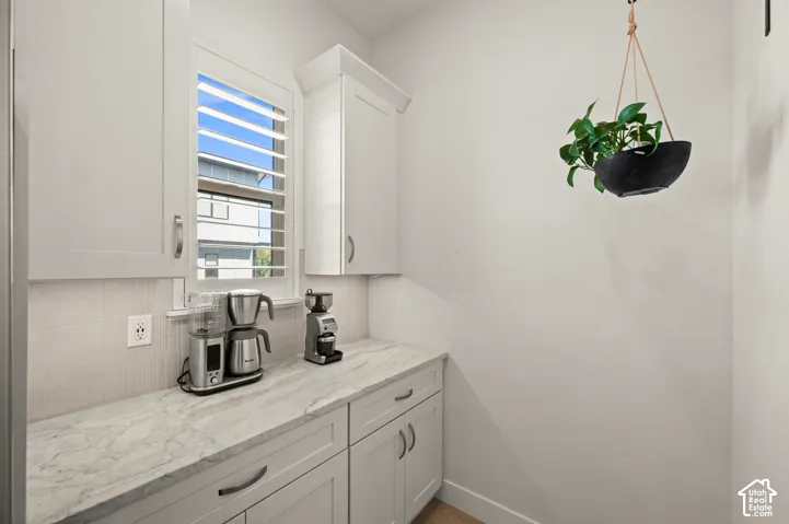 Tucked around the corner in the kitchen, this appliance area  has white shaker cabinetry with crown molding, granite countertops, and light-toned tile backsplash