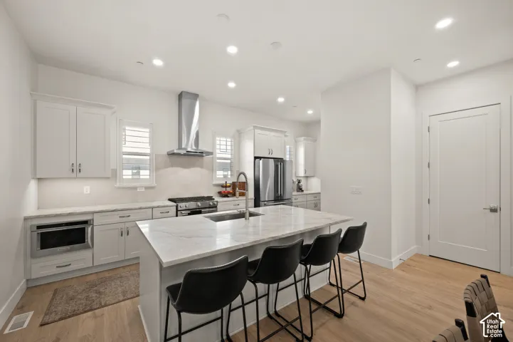 Central island with integrated sink, light-toned cabinetry, stainless steel appliances, granite countertops, recessed lighting, and wood-finish flooring