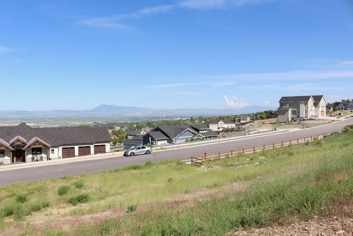 Mountain backdrop, distant city, residential street, sloped grassy terrain, and clear skies