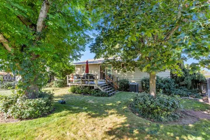 Expansive backyard featuring a manicured lawn, wood deck, and mature trees