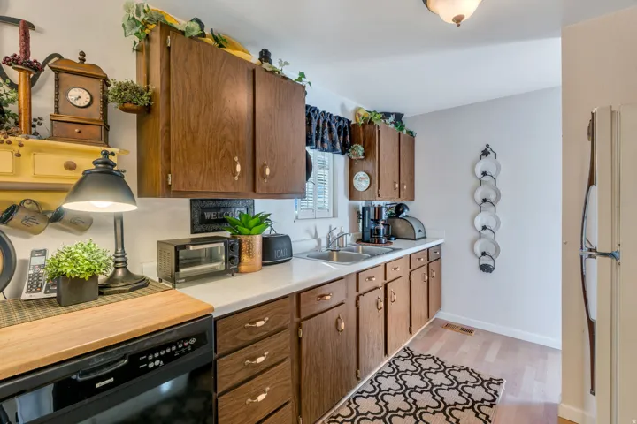 Wood-finish cabinetry, white countertops, built-in dishwasher, stainless steel double basin sink, and wood-finish flooring