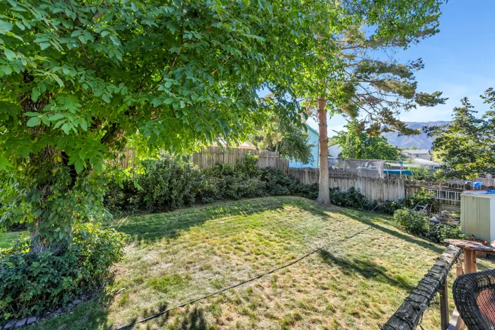 Expansive backyard featuring a sloped lawn, mature trees, and a wooden privacy fence