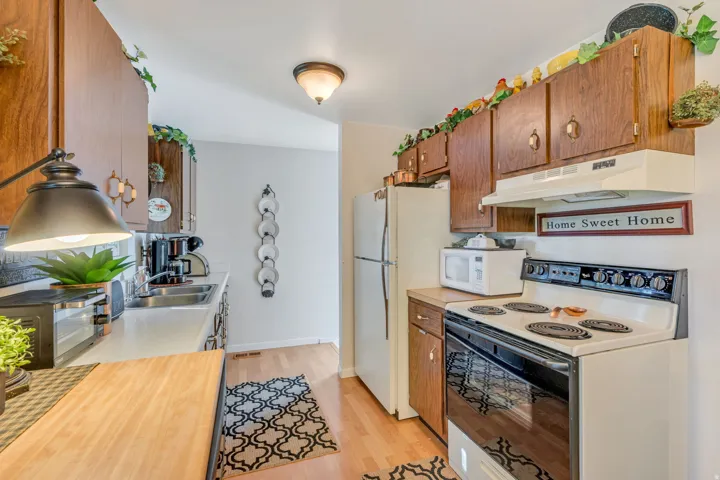 Wood-finish cabinetry with decorative hardware, compact refrigerator, and built-in electric range with exhaust hood