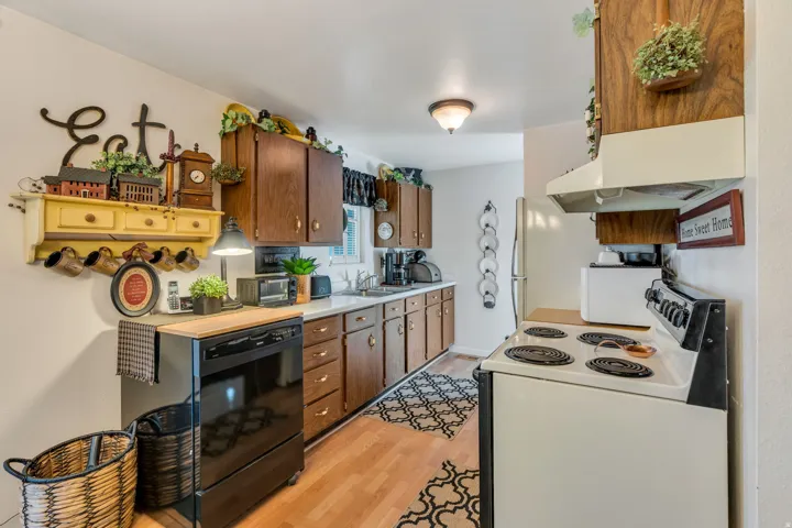 Kitchen featuring wood-finish cabinetry, white countertops, a black dishwasher, and wood-finish flooring