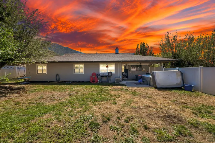 Backyard featuring a covered patio, a concrete slab, a white privacy fence, and mature trees