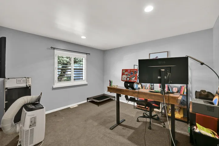 Recessed ceiling lighting, a window with plantation shutters, and light gray wall paint