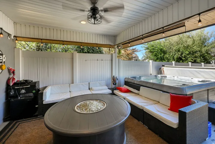 Covered patio featuring a ceiling fan, a built-in spa, track lighting, and a privacy fence