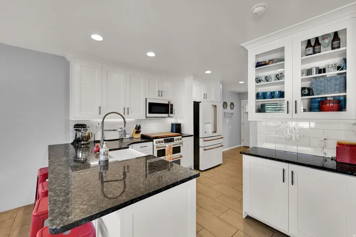 Kitchen featuring white shaker-style cabinetry, dark stone countertops, stainless steel appliances, a white subway tile backsplash, and wood-finish flooring