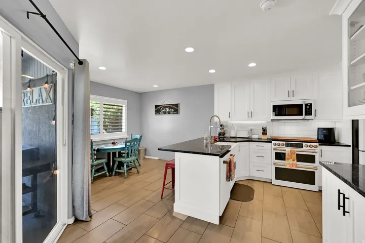 White cabinetry with dark countertops, a built-in microwave, and recessed lighting