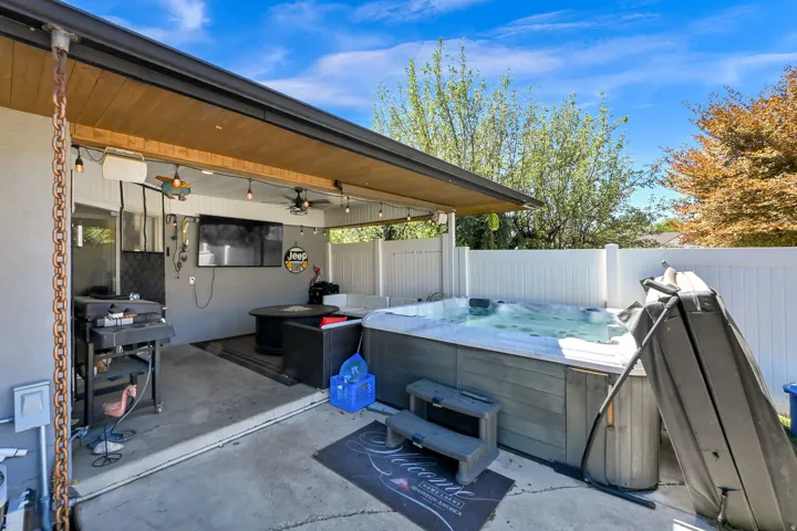 Covered outdoor living space featuring a large hot tub, built-in outdoor kitchen with grill, and privacy fencing