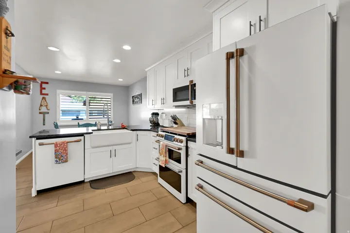 White cabinetry, black countertops, wood-finish flooring, white farmhouse sink, and stainless steel appliances