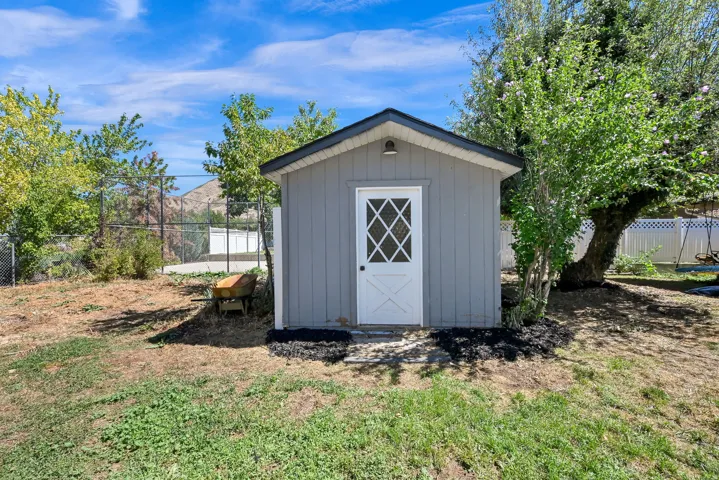 Storage shed with gray siding, a black shingled roof, and a white door with diamond-pane glass